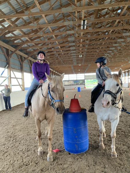 2 participants on horses smiling next to a barrel